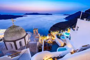 Imagen de las típicas casas blancas con techos azules de Santorini, con el mar Egeo y un hermoso atardecer en el fondo.