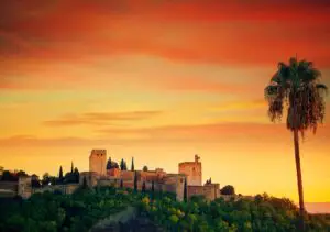 Fotografía de la Alhambra de Granada con el sol poniente en el fondo, representando uno de los principales atractivos turísticos de la ciudad, que se puede visitar en un viaje desde Barcelona a Granada.