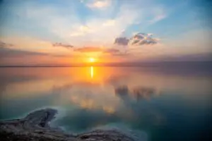 Imagen de la vista panorámica del Mar Muerto y las montañas en la distancia en Jordania, con una persona flotando en el agua y disfrutando de la experiencia de flotar en el agua salada.